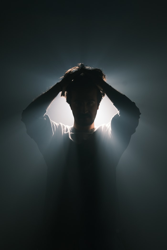 Man in darkness with hands on his head — representing stress
